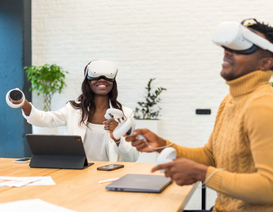 Business conference in VR in an office. A black man and woman using VR glasses and controllers, papers and gadgets on the table