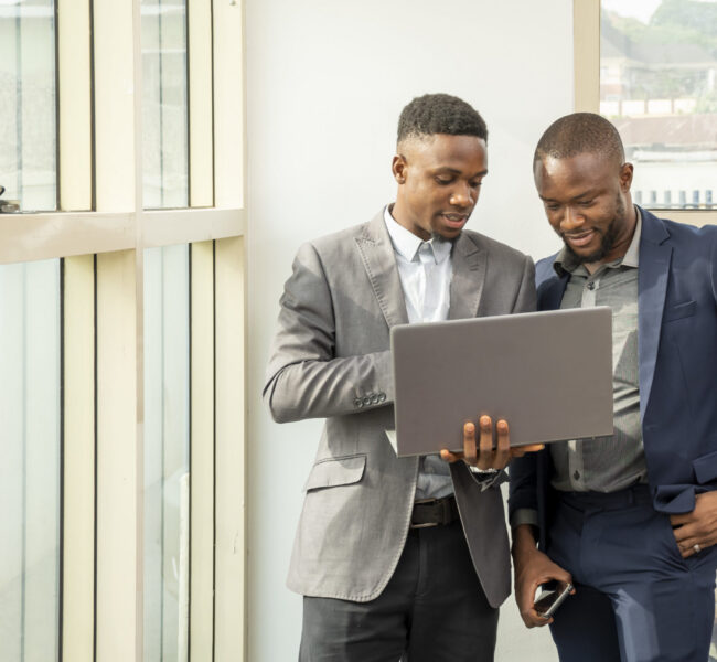 Two young black businessmen standing together holding a laptop, discussing business